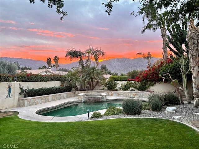 pool at dusk featuring a mountain view, an in ground hot tub, and a yard