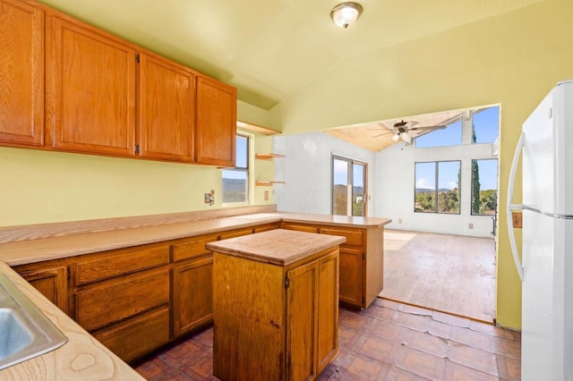 kitchen with kitchen peninsula, vaulted ceiling, a center island, white fridge, and ceiling fan