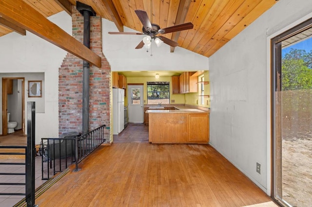 kitchen featuring beam ceiling, white fridge, kitchen peninsula, and a wood stove