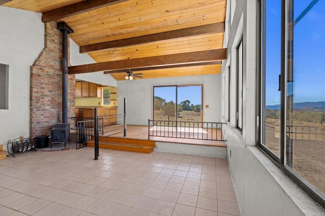 sunroom featuring vaulted ceiling with beams, a wood stove, wood ceiling, and ceiling fan