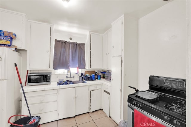 kitchen featuring decorative backsplash, sink, light tile patterned flooring, white cabinets, and gas stove