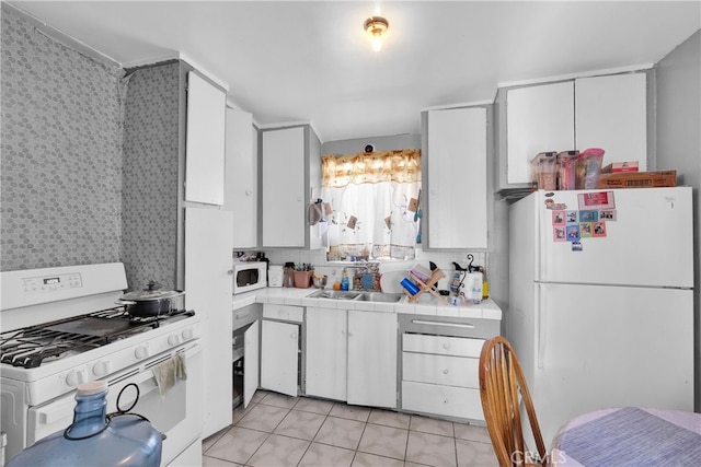 kitchen featuring tile countertops, white cabinetry, light tile patterned flooring, sink, and white appliances