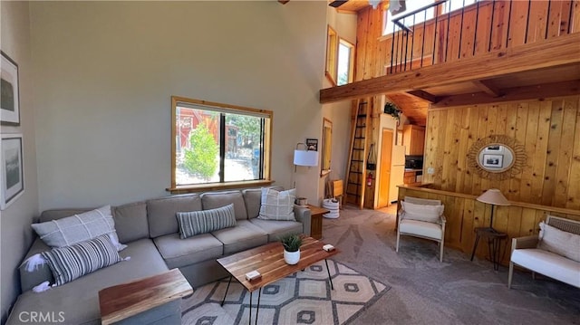 carpeted living room with a high ceiling, wood walls, and beamed ceiling