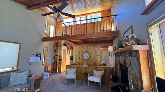 carpeted living room with ceiling fan, wooden ceiling, beamed ceiling, and wooden walls