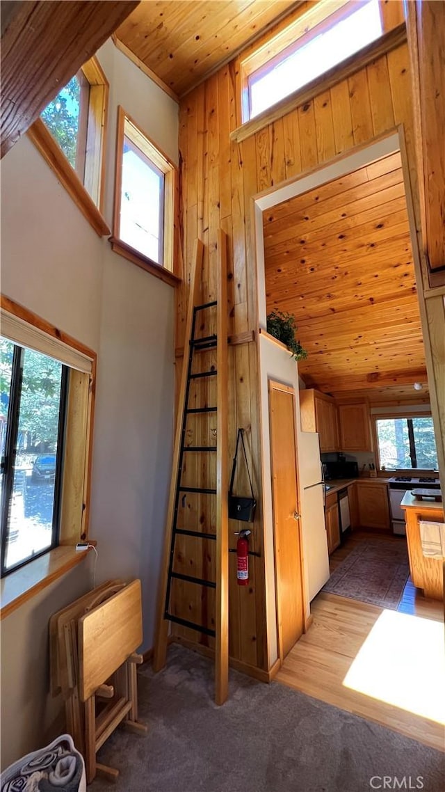 kitchen with light colored carpet, a towering ceiling, wooden walls, wood ceiling, and white refrigerator