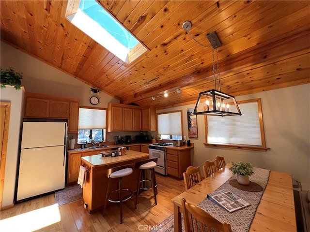 kitchen with pendant lighting, a center island, sink, white appliances, and light hardwood / wood-style flooring