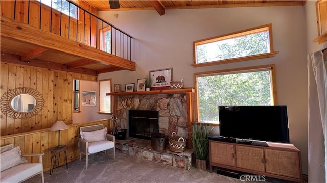 carpeted living room with wood ceiling, a stone fireplace, wood walls, high vaulted ceiling, and beam ceiling