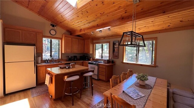 kitchen with a kitchen island, sink, white appliances, hanging light fixtures, and light wood-type flooring