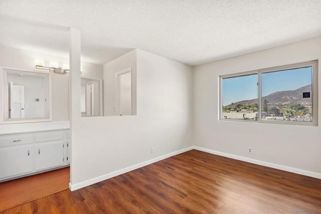 unfurnished room with a mountain view, a textured ceiling, and hardwood / wood-style floors