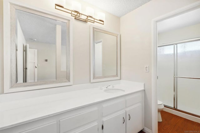 bathroom featuring hardwood / wood-style floors, a shower with door, a textured ceiling, toilet, and vanity