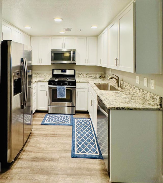 kitchen featuring light stone counters, stainless steel appliances, sink, and white cabinets