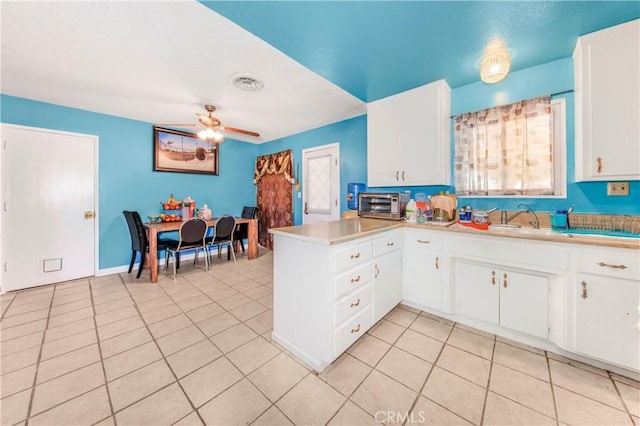 kitchen with light tile patterned floors, a ceiling fan, a peninsula, a sink, and light countertops