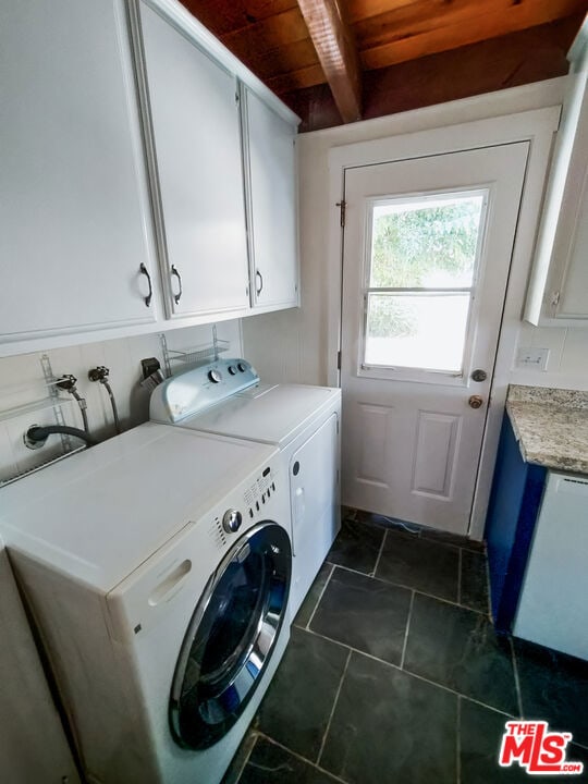 clothes washing area with washer and clothes dryer, cabinets, wooden ceiling, and dark tile patterned flooring