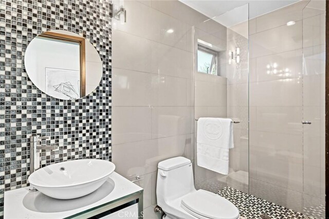 bathroom with a tile shower, tile walls, backsplash, vanity, and toilet