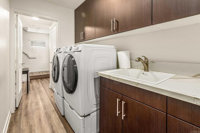 laundry area featuring sink, light hardwood / wood-style flooring, washing machine and dryer, and cabinets