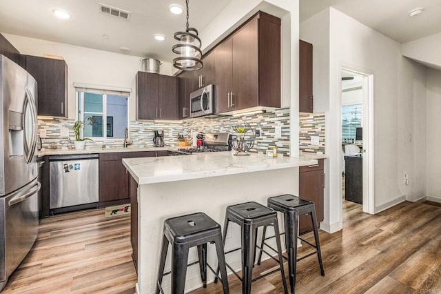 kitchen featuring decorative backsplash, a breakfast bar area, dark brown cabinets, stainless steel appliances, and light hardwood / wood-style floors