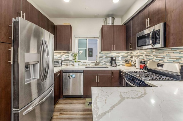 kitchen featuring backsplash, light stone countertops, light wood-type flooring, sink, and stainless steel appliances