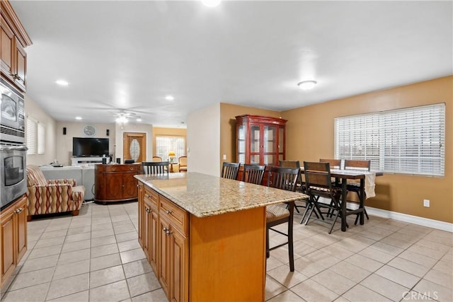 kitchen with a breakfast bar, a center island, stainless steel oven, ceiling fan, and light stone counters