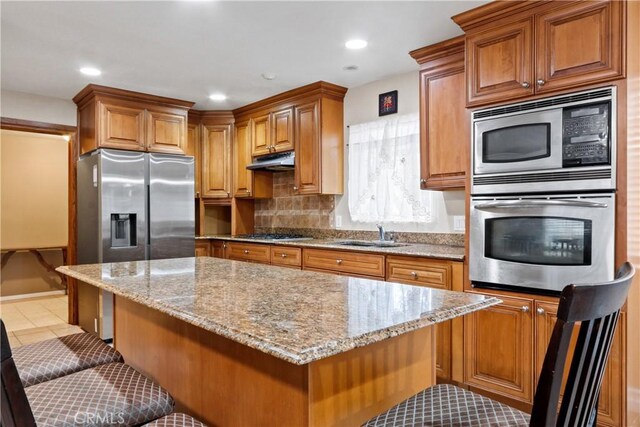 kitchen featuring a kitchen bar, stainless steel appliances, light stone countertops, and light tile patterned flooring