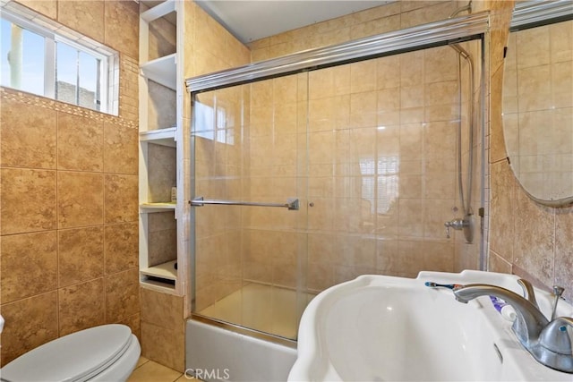 full bathroom with tile patterned floors, bath / shower combo with glass door, sink, tile walls, and toilet