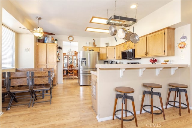 kitchen with light brown cabinets, a kitchen breakfast bar, appliances with stainless steel finishes, light hardwood / wood-style floors, and ceiling fan