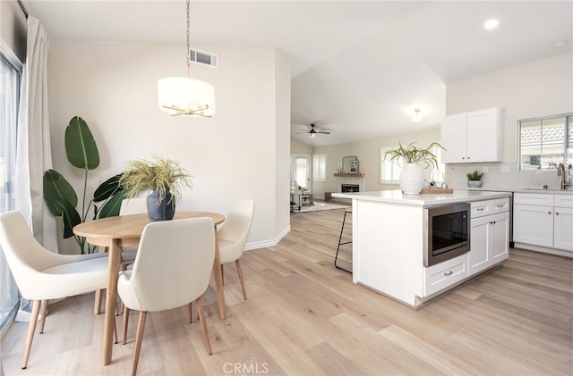 kitchen featuring light hardwood / wood-style floors, stainless steel microwave, white cabinets, and pendant lighting