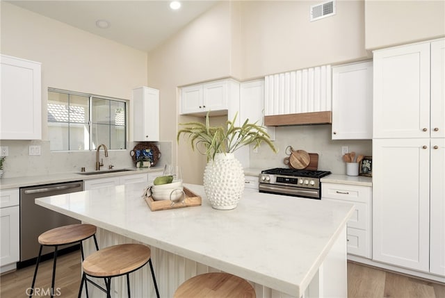 kitchen with a kitchen breakfast bar, stainless steel appliances, sink, a center island, and white cabinetry