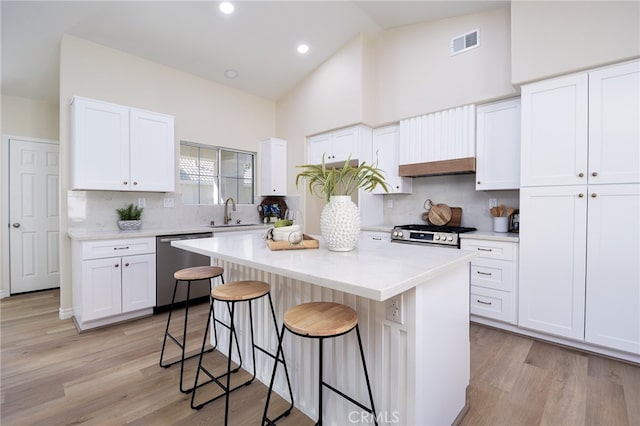 kitchen with appliances with stainless steel finishes, a kitchen island, white cabinetry, and light wood-type flooring