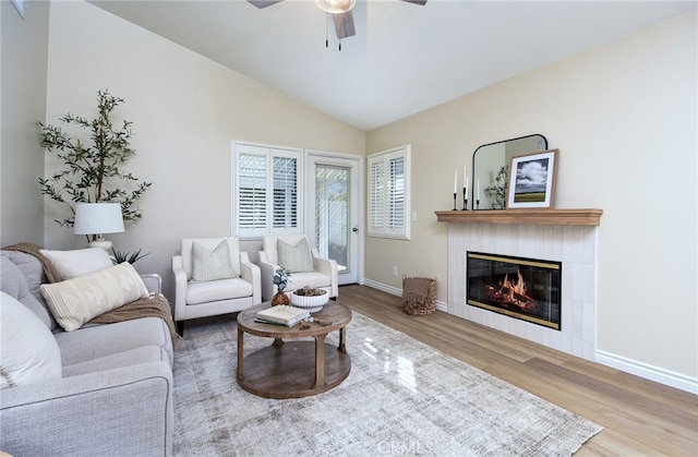 living room with vaulted ceiling, a tiled fireplace, wood-type flooring, and ceiling fan