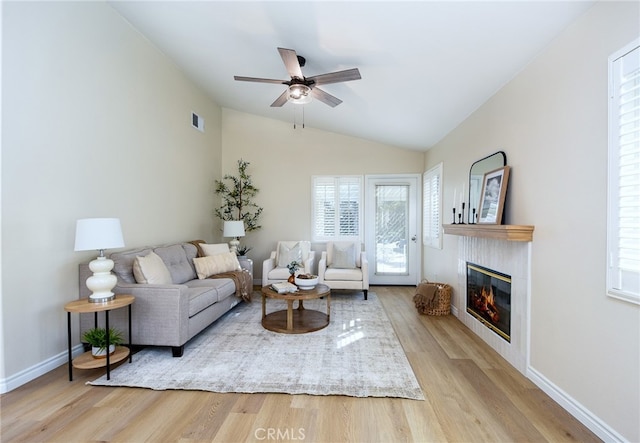 living room with lofted ceiling, a tile fireplace, light wood-type flooring, and ceiling fan