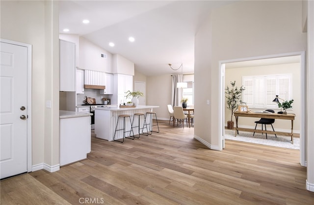 kitchen with hanging light fixtures, a center island, a kitchen bar, light wood-type flooring, and white cabinets