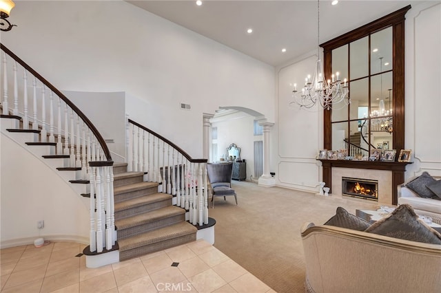 carpeted entryway featuring a premium fireplace, ornate columns, and a towering ceiling