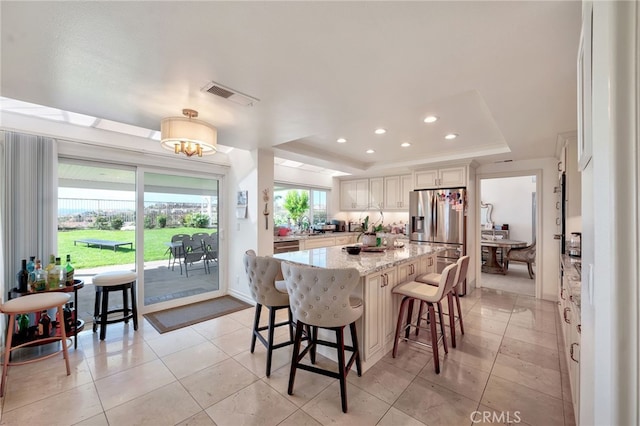 kitchen with light stone countertops, a kitchen bar, a kitchen island, a tray ceiling, and stainless steel refrigerator with ice dispenser