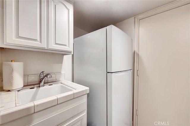 kitchen featuring tile counters, white cabinetry, white fridge, and sink