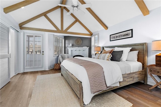 bedroom with access to exterior, ceiling fan, hardwood / wood-style flooring, a fireplace, and vaulted ceiling with beams