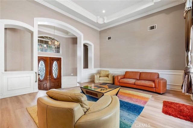 living room featuring french doors, light wood-type flooring, crown molding, an inviting chandelier, and a high ceiling