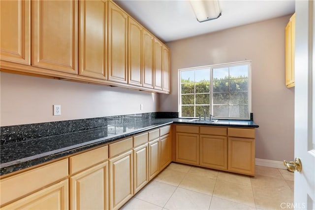 kitchen featuring light tile patterned floors, sink, light brown cabinetry, and dark stone counters