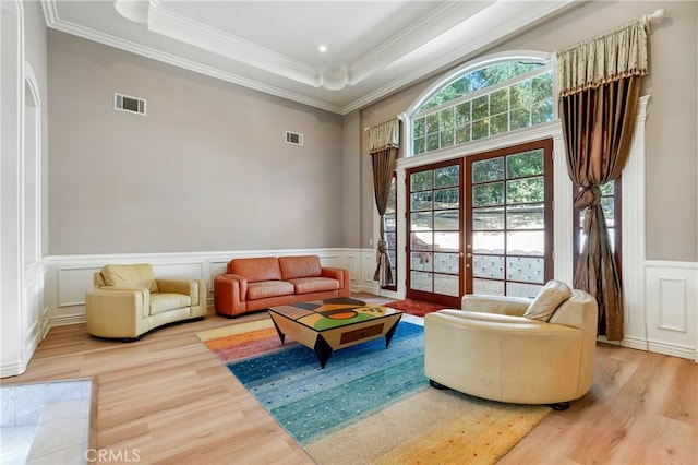 living room with a tray ceiling, crown molding, french doors, and wood-type flooring