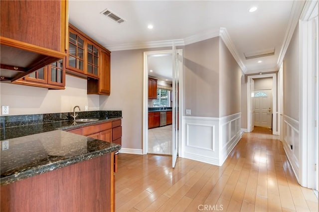 kitchen featuring sink, dark stone countertops, ornamental molding, stainless steel dishwasher, and light wood-type flooring