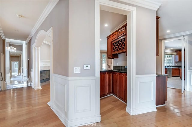 hall featuring decorative columns, sink, ornamental molding, light hardwood / wood-style floors, and a chandelier