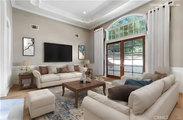 living room featuring a high ceiling, a tray ceiling, light hardwood / wood-style floors, ornamental molding, and french doors