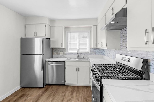 kitchen with sink, hardwood / wood-style flooring, appliances with stainless steel finishes, light stone counters, and white cabinets