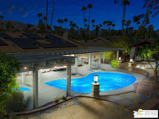 pool at night featuring exterior bar and a patio