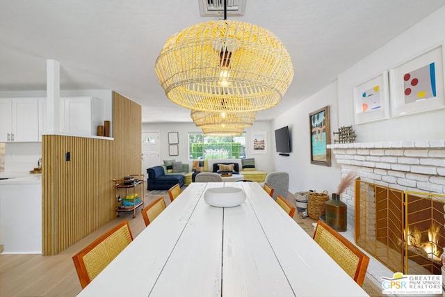 dining room with light hardwood / wood-style floors, a brick fireplace, and a notable chandelier