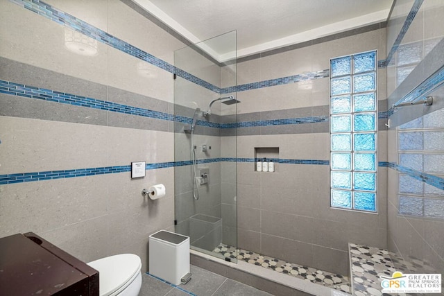 bathroom with a tile shower, plenty of natural light, tile walls, and toilet