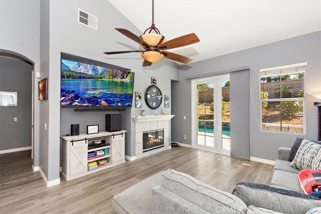 living room with a tiled fireplace, ceiling fan, vaulted ceiling, and light wood-type flooring