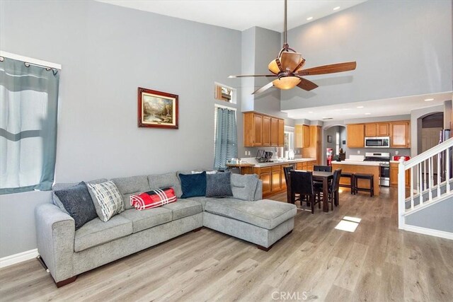 living room featuring a towering ceiling, light hardwood / wood-style flooring, and ceiling fan