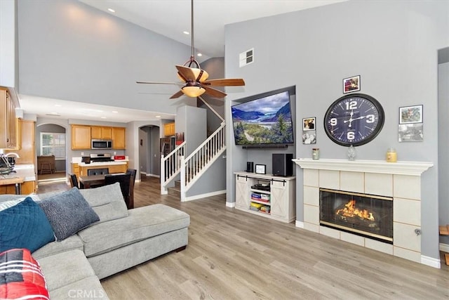 living room featuring a fireplace, light hardwood / wood-style floors, high vaulted ceiling, and ceiling fan