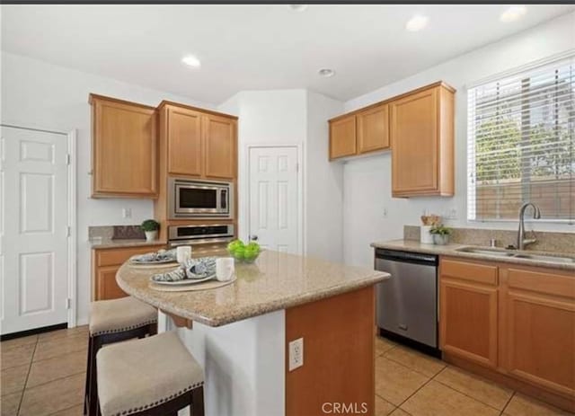 kitchen with sink, light tile patterned floors, light stone counters, a kitchen island, and appliances with stainless steel finishes