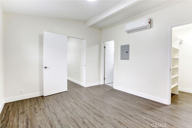 spare room featuring a wall mounted AC, baseboards, electric panel, wood finished floors, and lofted ceiling with beams